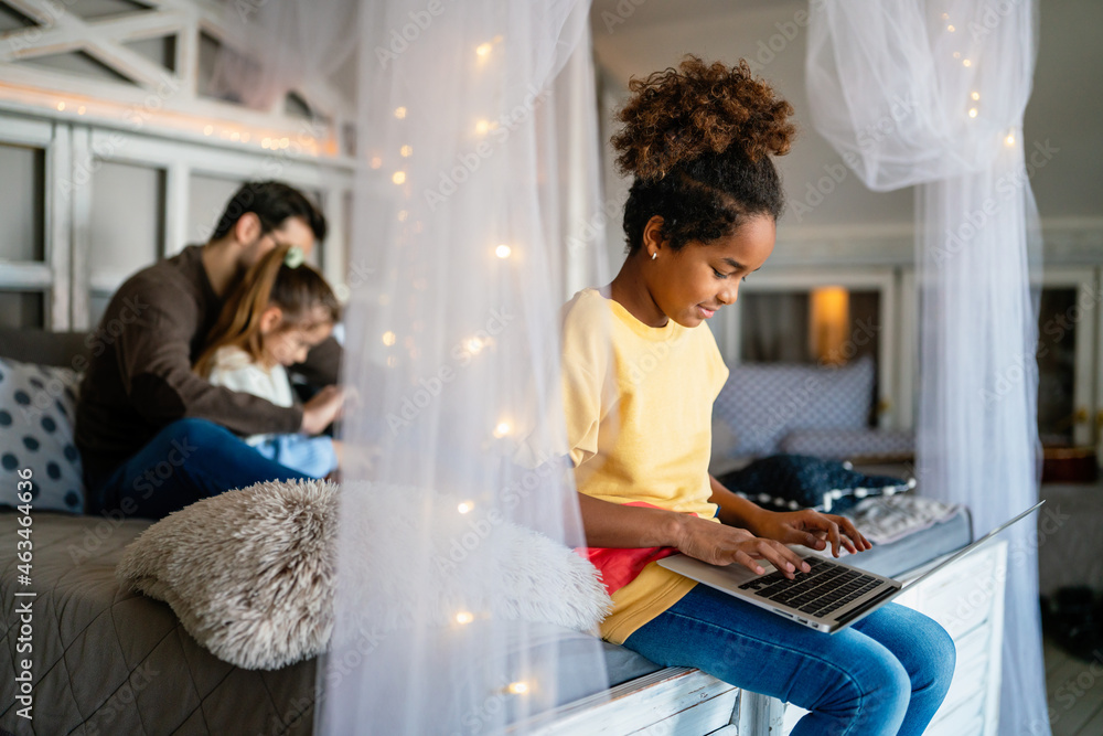 Wall mural Preteen schoolgirl doing her homework with notebook at home. Child using gadgets to study.