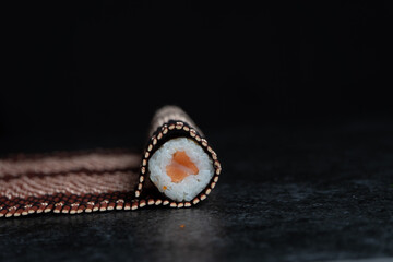 sushi roll wrapped in bamboo tablecloth on a black stone background