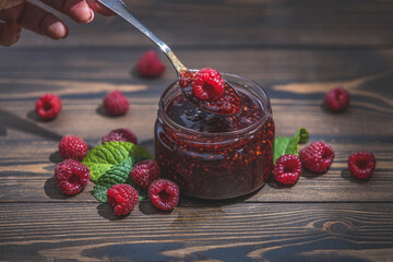Homemade raspberry jam or marmalade in the glass jar and ripe raspberry on the wooden table