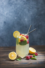 Glass of cold icy refreshing drink with lemon and raspberry served on dark wooden table surface