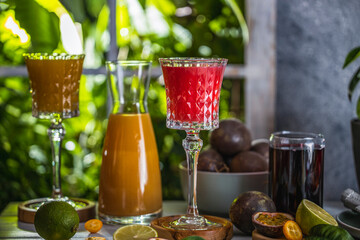 Two elegant glasses of mango, kumquat and passiflora liqueur on light gray table surface near window with sunny light