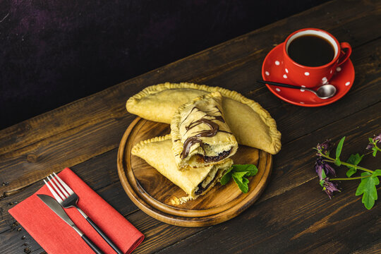 Breakfast with sweet chocolate sandwich-sized calzone  and coffee served on dark wooden table.