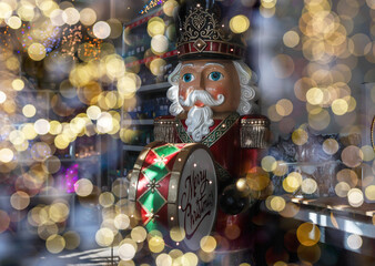 Big nutcracker toy drummer among blurred Christmas lights.