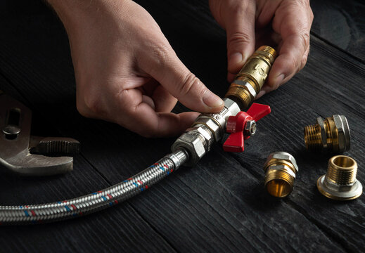 The plumber connects brass fittings to plumbing hose. Close-up of hand of the master during work in workshop.