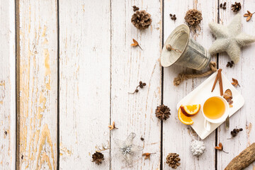 Christmas background with a warming cup of tea and natural decoration like pine cones, nuts, Christmas bell and a star on a light, rustic wooden background in vintage style