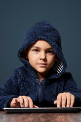 A little kid with a hoodie typing computer keyboard. Cute multi-racial 8-years old boy wearing...