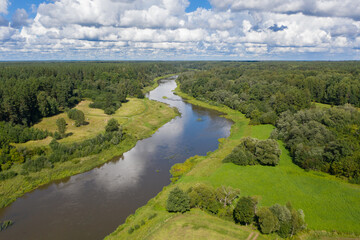 Aerial view of river flowing through green forest. Cloudy sky