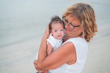 Grandma holding newborn baby boy at the beach