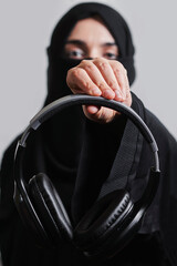 Muslim woman in traditional hijab clothing holding black wireless headphones