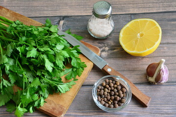 green parsley on cutting board with lemon and spices on wooden background, food design