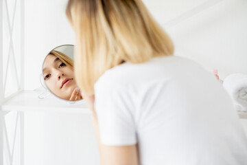 Obraz na płótnie Canvas Facial care. Skin treatment. Morning routine. Attractive young woman with perfect clean face in mirror reflection at light background.