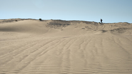 Fototapeta na wymiar Unrecognized person walking in sand dunes dry land in midday