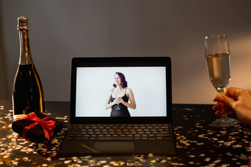 Happy birthday. Video greeting. Home holiday. Unrecognizable woman with glass champagne looking female friend congrats on laptop in dark room interior.