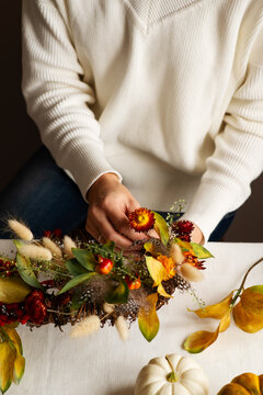 Woman hands with diy floral autumn wreath with driad grass, plant and berry