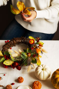Woman hands with diy floral autumn wreath with driad grass, plant and berry