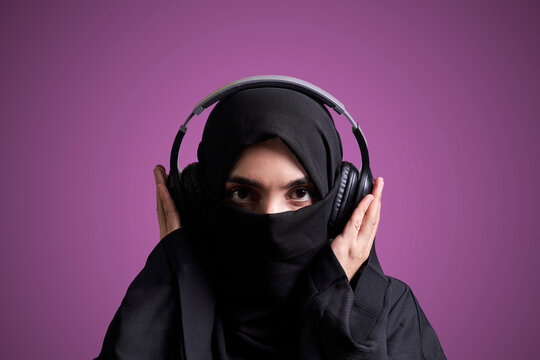Muslim woman in hijab listening to music with wireless headset. Arabic girl in traditional nikab clothing listening favorite music with wireless headphones
