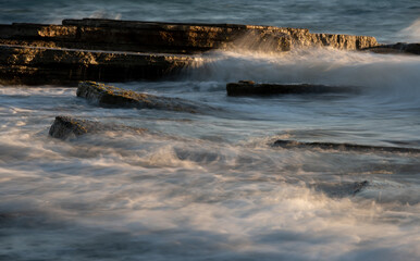 Stormy windy sea waves splashing on a rocky seashore at sunset