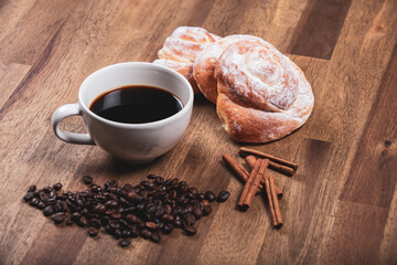 Desayuno con café, ensaimadas, canela en rama y granos de café sobre mesa de madera