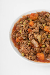 Vegan stew with seitan, carrot, green peas and onion on a white plate. White background, close view. 
