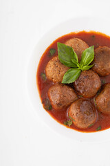 Vegan meatballs with tomato sauce and basil leaf on a white plate. White background, close view