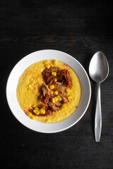 Vegan corn cream soup with seitan, spoon laying aside on black wooden background. Top view.