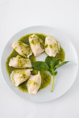 Vegan potato dumplings with pesto sauce on a white plate. White background, top view.