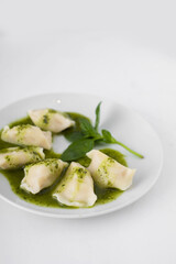 Vegan potato dumplings with pesto sauce on a white plate. White background, close view.