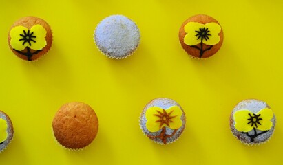 Rows of muffins decorated with powdered sugar and yellow flower shaped icing on a yellow background