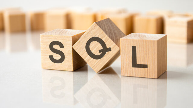 three wooden cubes with the letters SQL on the bright surface of a gray table, business concept