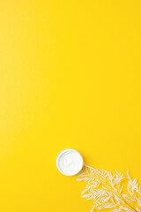 Jar of cosmetic cream with flowers on yellow background. Flat lay, copy space