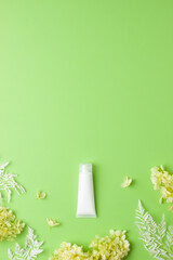 White tube of cosmetic cream with flowers on green background. Flat lay, copy space