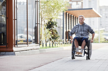 Fototapeta na wymiar Mature man with disability riding in wheelchair outdoors he walking on fresh air