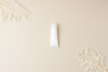 White tube of cosmetic cream with flowers on pastel beige background. Flat lay, copy space