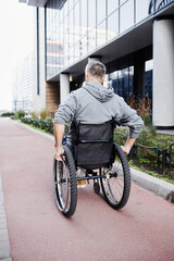 Rear view of mature male patient riding in wheelchair along the street outdoors