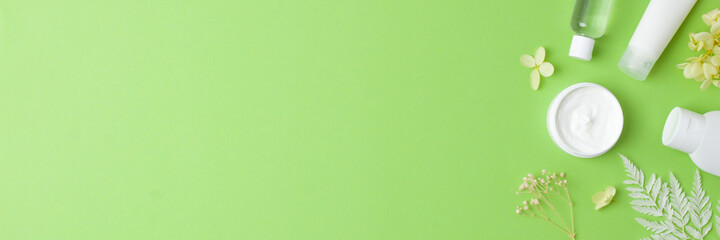 Cosmetic skin care products with with flowers on green background. Flat lay, copy space