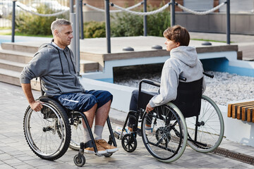 Obraz premium Mature couple sitting in wheelchairs opposite each other and talking while spending time on fresh air