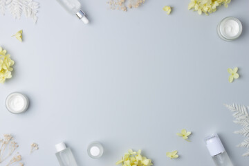 Cosmetic skin care products with with flowers on grey background. Flat lay, copy space