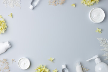 Cosmetic skin care products with with flowers on grey background. Flat lay, copy space