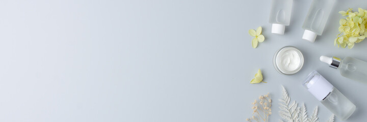 Cosmetic skin care products with with flowers on grey background. Flat lay, copy space