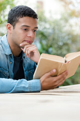 young student reading book outdoors