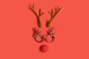 Funny Christmas face with antlers of a deer, toy glasses and a clown nose on a red background