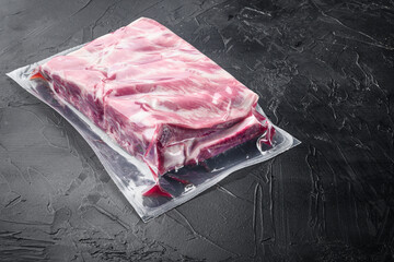 Fresh Pork rib in plastic pack, on black stone background, with copy space for text