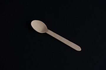 One wooden disposable spoon made from birch tree lies on black background. Selective focus. Biodegradable cutlery. Nature pollution reduction theme.