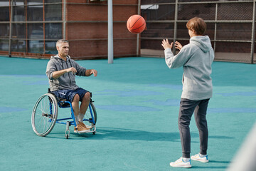 Paraplegic mature man in wheelchair throwing the ball to woman they training on the sport ground...