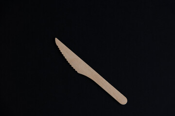 One wooden disposable knife made from birch tree lies on black background. Selective focus. Biodegradable cutlery. Nature pollution reduction theme.