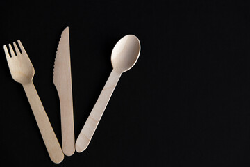 Set of wooden disposable biodegradable cutlery (spoon, fork and knife) lies on black background....
