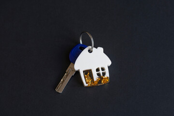 Close-up view of white house shaped keychain with gold sequins made from epoxy resin lying on black...