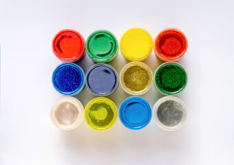 Color glitter paints in jars on a white background. Top view.