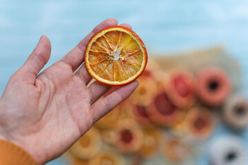 dried orange slice in a hand for diy projects, gift wrapping and beautiful eco Christmas decorations like wreaths, more decoration items arranged on a blue wooden table in the background - 463489062