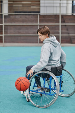 Mature Paraplegic Woman Sitting In Wheelchair Playing Basketball On Sport Ground